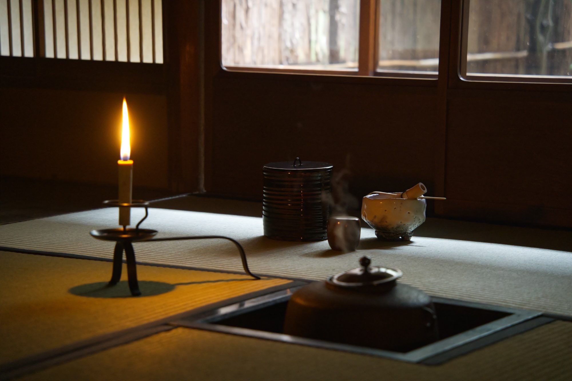 A candle beside tea utensils and the sunken hearth